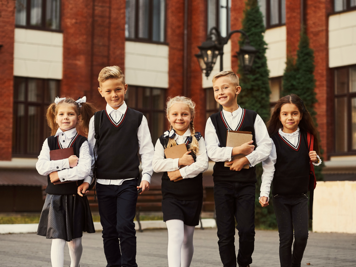 5 kids in school uniforms walking in front of school.