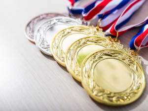 1st, 2nd, 3rd place medals stacked on table with red, white and blue ribbons attached.