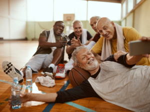 Group of active male seniors sitting on court together posing fo r photo after playing basketball.