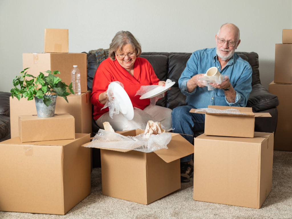 Senior couple sitting on couch packing and sorting items into boxes.