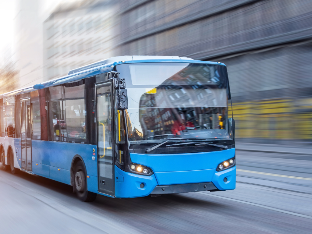 Generic blue bus driving through city streets so fast that background is blurred.