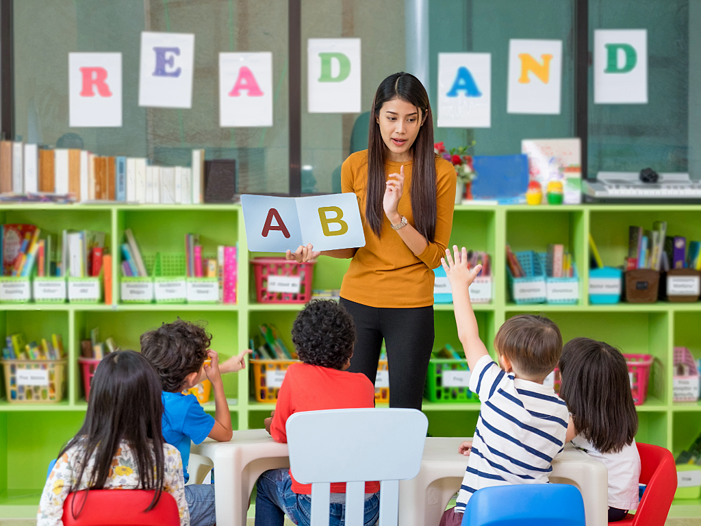 Young woman holding up letters of the alphabet teaching preschoolers.